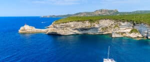 a white catamaran sailing on blue sea water along coast of corsica island, france