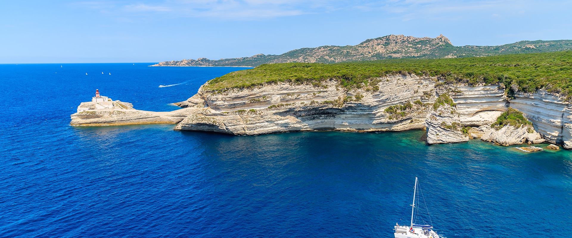 a white catamaran sailing on blue sea water along coast of corsica island, france